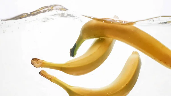 Nahaufnahme von frischen reifen Früchten, die ins Wasser fallen. Gelbe süße Babanen planschen und fließen im Wasser vor weißem Hintergrund — Stockfoto