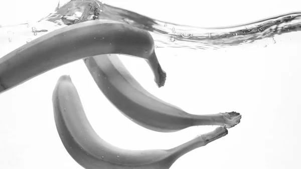 Fechar imagem em preto e branco de banas maduras frescas caindo e salpicando. Frutos saborosos flutuando na água — Fotografia de Stock
