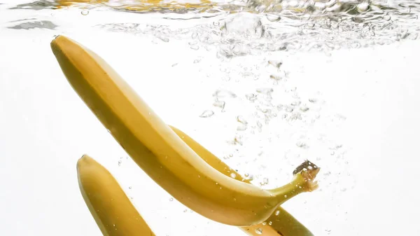 Foto de close-up de bananas amarelas maduras frescas caindo e salpicando em água clara contra o backgorund branco isolado — Fotografia de Stock