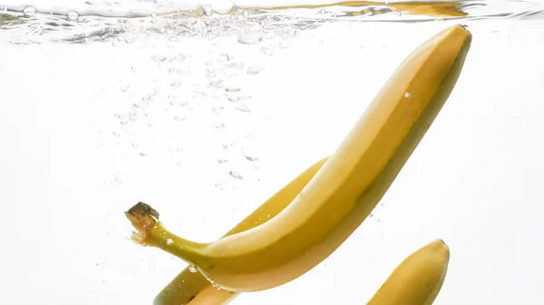 新鲜成熟的香蕉在白色孤立背景下在水中掉落和溅起的特写图像 — 图库照片