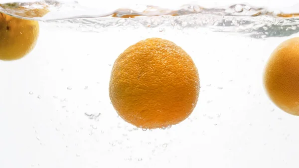 Imagen de cerca de naranjas frescas maduras que caen y salpican en el agua contra el fondo blanco — Foto de Stock