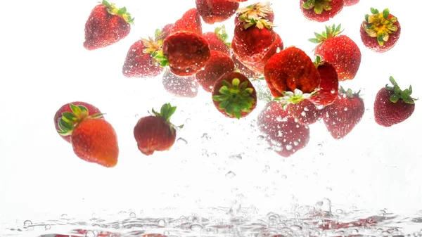 Foto de primer plano de un montón de fresas frescas maduras flotando en agua clara con burbujas de aire sobre fondo blanco — Foto de Stock