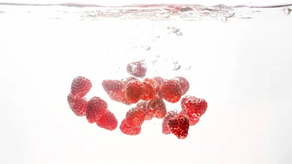 Крупный план изображения большого количества свежей спелых вкусных красных малины с пузырьками воздуха в чистой воде на изолированном белом фоне — стоковое фото