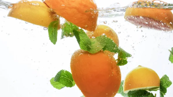 Imagen de cerca de naranjas jugosas frescas cortadas con hojas de menta flotando en agua clara sobre fondo blanco — Foto de Stock