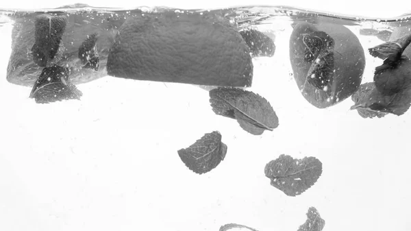 Turuncu ve nane yaprakları nın siyah ve beyaz yakın çekim görüntüsü suda yüzer. Düşen ve su sıçrayan meyveler — Stok fotoğraf