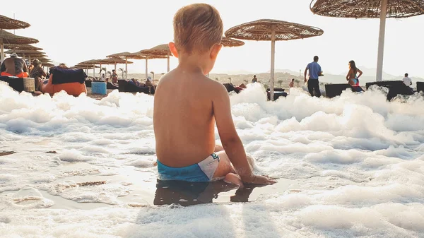 Zbliżenie zdjęcie z małym 3 lat chłopiec Toddler siedzi na piaszczystej plaży i grając z dużą ilością mydła po plaży Disco party — Zdjęcie stockowe