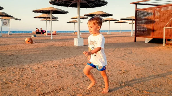 Portret szczęśliwego uśmiechniętego chłopca malucha biegnąc na piaszczystej plaży morskiej. Dziecko bawią się i odprężą na letnich wakacjach — Zdjęcie stockowe