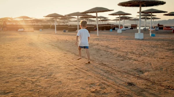 Photo tonique de l'adorable garçon tout-petit de 3 ans courant sur la plage de la mer vers le soleil couchant sur le rivage — Photo