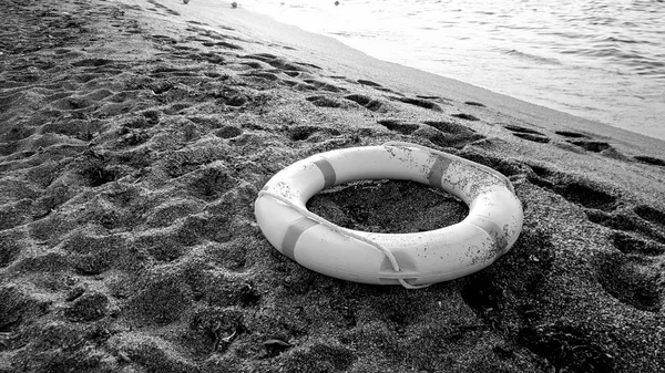 Μαύρη και λευκή εικόνα από πλαστικό δαχτυλίδι εξοικονόμησης ζωής που βρίσκεται στην παραλία της θάλασσας. Έννοια της ασφάλειας κατά τη διάρκεια των καλοκαιρινών διακοπών στην παραλία — Φωτογραφία Αρχείου