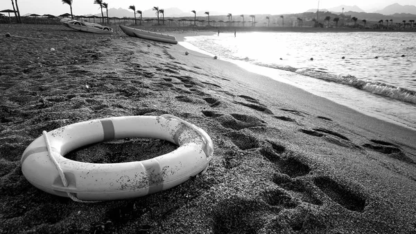 Μαύρη και λευκή εικόνα από πλαστικό δαχτυλίδι εξοικονόμησης ζωής που βρίσκεται στην παραλία της θάλασσας. Έννοια της ασφάλειας κατά τη διάρκεια των καλοκαιρινών διακοπών στην παραλία — Φωτογραφία Αρχείου