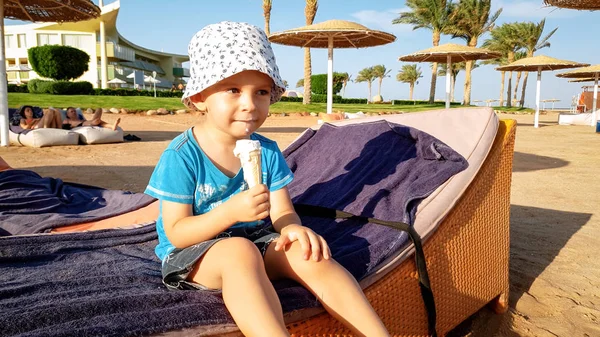 Portret adorable 3 lat chłopiec maluch siedzi na plaży i jeść smaczne słodkie lody. Dziecko relaks na letnich wakacji wakacje na plaży — Zdjęcie stockowe