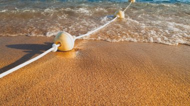 Kumlu deniz kıyısında yüzen şamandıralar üzerinde yuvarlanan ve frenleme sakin deniz dalgaları closeup görüntü