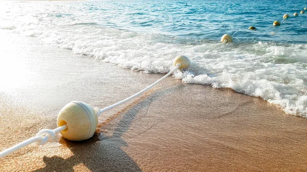Κοντινά πλάνα όμορφη εικόνα της μεγάλης γραμμής των αιωρούμενα σημαδούρες που συνδέονται με το σχοινί που επιπλέει στη θάλασσα και βρίσκεται στην αμμώδη παραλία — Φωτογραφία Αρχείου