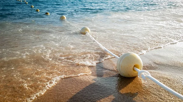 Closeup image of calm sea waves rolling and braking on the floating buoys on the sandy sea shore — Stock Photo, Image