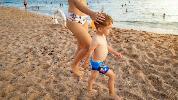 Imagem bonita de feliz sorrindo menino de 3 anos de idade criança andando e relaxando na praia de areia ao pôr do sol. Família se divertindo durante as férias na praia de verão — Fotografia de Stock