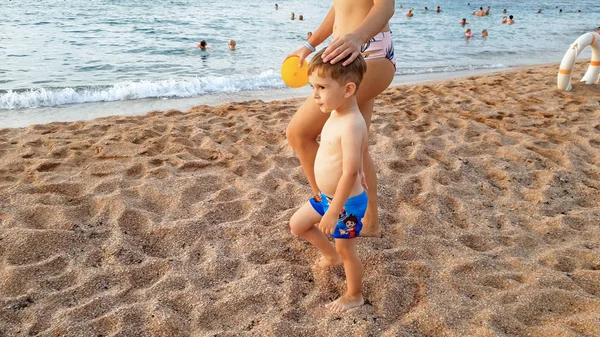 Piękne zdjęcie szczęśliwej młodej matki trzymające jej małe dziecko chłopca przez rękę i chodzenie na sndy plaży morza w ciepłych spokojnych fal przed niesamowitym Niebo Zachód słońca — Zdjęcie stockowe