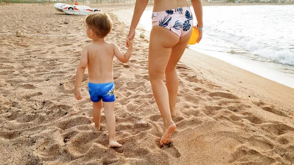 Wizerunek szczęśliwej młodej matki z adorable 3 lat chłopiec Toddler trzymając ręce i chodzenie na plaży morskiej przed pięknym Niebo Zachód słońca nad powierzchnią wody — Zdjęcie stockowe