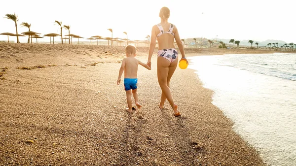Hermosa imagen de feliz sonriente niño de 3 años caminando y relajándose en la playa de arena al atardecer. Familia pasar un buen rato durante las vacaciones de vacaciones de verano playa —  Fotos de Stock