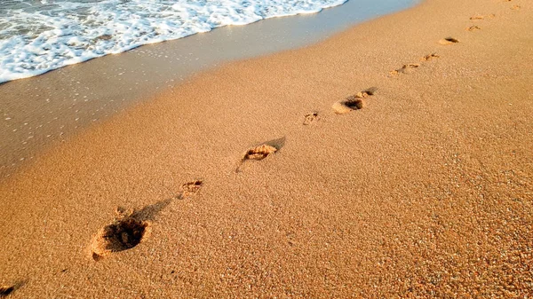 Primer plano hermosa imagen de huellas humanas en la arena mojada en la playa del mar contra el hermoso atardecer sobre la superficie del agua — Foto de Stock