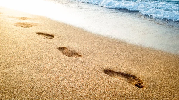 Primer plano hermosa imagen de huellas humanas en la arena mojada en la playa del mar contra el hermoso atardecer sobre la superficie del agua —  Fotos de Stock