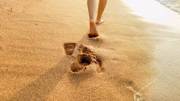 Closeup image of sexy barefoot female feet walking on the wet sand and calm warm waves at sea beach