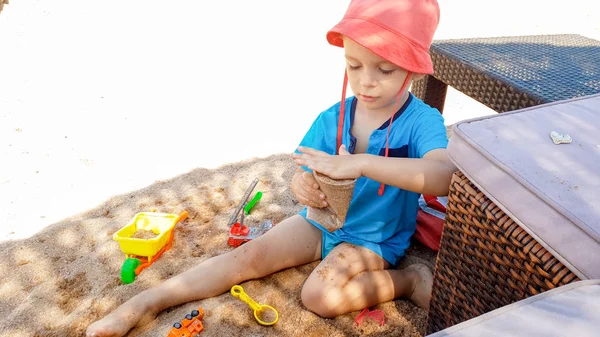 Portrait of cute 3 years old toddler boy sitting on the sandy beach and playing with toys and building sand castle — Stock Photo, Image
