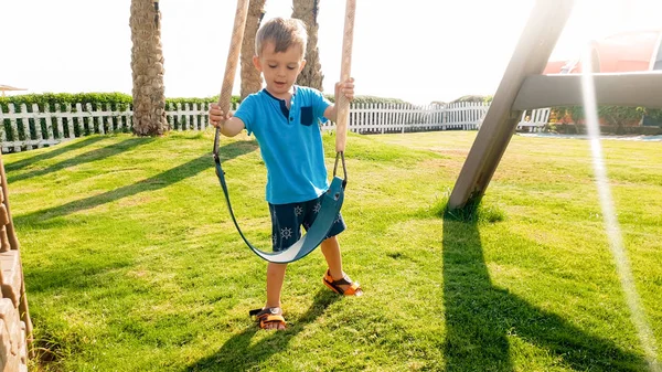 Photo of adorable smiling little boy playing with chaing swing on the playground. Active baby playing and having outdoors at park — Stock Photo, Image