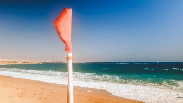 Κοντινό πλάνο της κόκκινης σημαίας που φτερουγίζει στον άνεμο στην παραλία της θάλασσας. Έννοια της ασφάλειας στη θάλασσα ή στον ωκεανό — Φωτογραφία Αρχείου