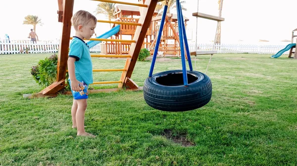 Imagem de menino pequeno bonito brincando com balanços no palyground no parque — Fotografia de Stock