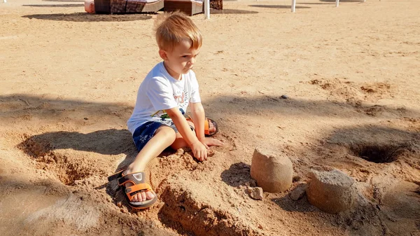 Portret cute 3 lat chłopiec chłopca siedzi na piaszczystej plaży i gry z zabawek i budynku zamek z piasku — Zdjęcie stockowe