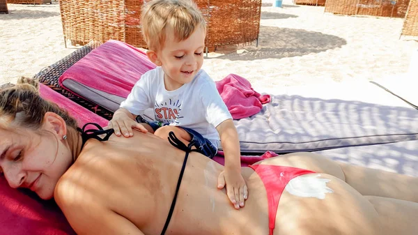 Foto von niedlichen 3 Jahre alten kleinen Jungen machen Massage für junge Mutter entspannen auf der Liege am Strand — Stockfoto