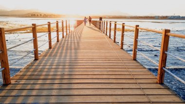 Sakin okyanus dalgaları ve uzun ahşap iskele güzel manzara. Dağların üzerinde gün batımına karşı denizde inanılmaz iskele