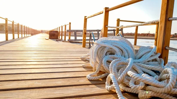 Closeup photo of ropes lying on the wooden deck of long pier at sea coast — Stock Photo, Image