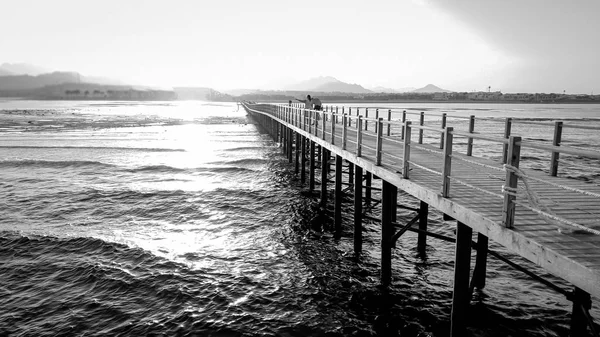 海洋长木码头的黑白图像。平静的海浪和令人惊叹的日落在山上 — 图库照片