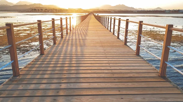 Amazing sunset over the long wooden pier in calm ocean. Sea waves rolling on breaking on the wooden bridge — Stock Photo, Image