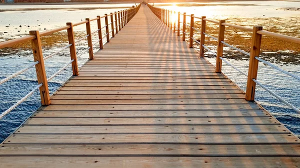 Hermoso paisaje de tranquilas olas oceánicas y largo muelle de madera. Increíble embarcadero en el mar contra el atardecer sobre las montañas — Foto de Stock