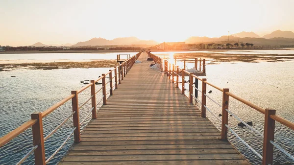 Hermoso paisaje de tranquilas olas oceánicas y largo muelle de madera. Increíble embarcadero en el mar contra el atardecer sobre las montañas — Foto de Stock