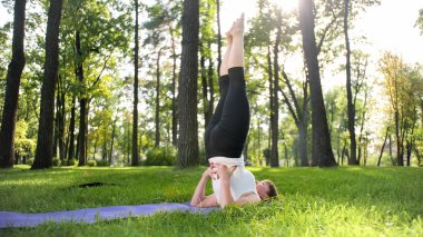 Germe ve yoga egzersizleri yapıyor fitness giysileri gülümseyen orta yaşlı kadın Görüntü. Kadın meditasyon ve parkta çim üzerinde fitness mat spor yapıyor