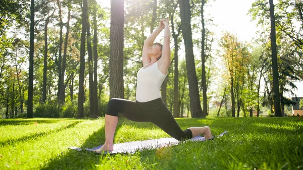 Photo of smiling happy woman 40 years old doing yoga exercises on fitness mat at forest. Harmony of human in nature. Middle aged people taking car of mental and physical health