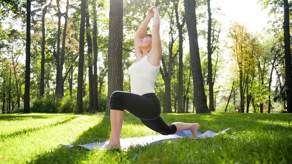 Imagen de mujer feliz sonriente de mediana edad meditando y haciendo ejercicios de yoga sobre hierba en el bosque. Mujer cuidando de su salud física y mental mientras practica fitness y estiramiento en el parque — Foto de Stock