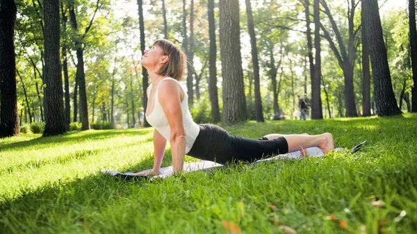 Foto de mulher sorridente de meia-idade praticando ioga asana. Persong meditando na natureza. Equilíbrio e harmonia de corpo e mente — Fotografia de Stock