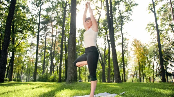 Photo of smiling happy woman 40 years old doing yoga exercises on fitness mat at forest. Harmony of human in nature. Middle aged people taking car of mental and physical health