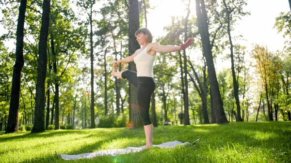 Zdjęcie uśmiechniętej kobiety robi jogi i ćwiczeń fitness. Ludzie w średnim wieku dbają o swoje zdrowie. Harmonia ciała i umysłu w przyrodzie — Zdjęcie stockowe