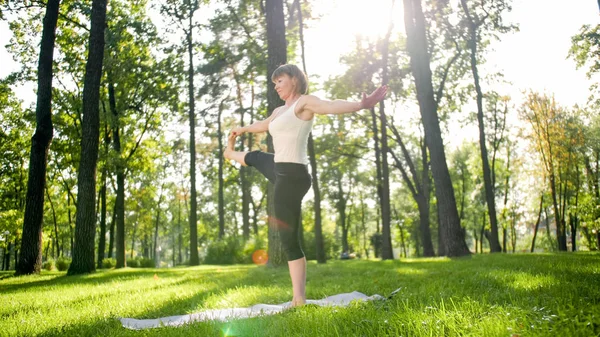 Photo of middle aged smiling woman practising yoga asana. Persong meditating in nature. Balance and harmony of body and mind