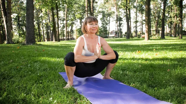 Foto de mulher sorridente fazendo exercícios de ioga e fitness. Pessoas de meia-idade cuidando de sua saúde. Harmonia de corpo e mente na natureza — Fotografia de Stock