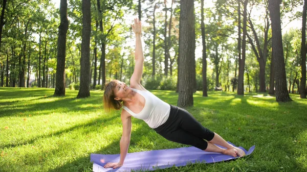 Фото женщины средних лет в спортивной одежде, практикующей йогу на открытом воздухе в парке. Женщина средних лет растягивается и медитирует в лесу — стоковое фото