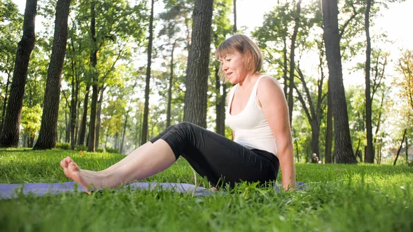 Photo de souriante femme heureuse de 40 ans faisant des exercices de yoga sur tapis de fitness à la forêt. Harmonie de la nature humaine. Personnes d'âge moyen prenant voiture de santé mentale et physique — Photo