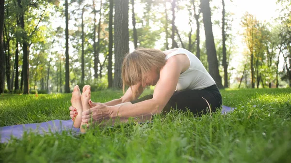 Photo d'une femme d'âge moyen souriante pratiquant le yoga et méditant au parc. Femme étirement et faire de remise en forme sur tapis à la forêt — Photo