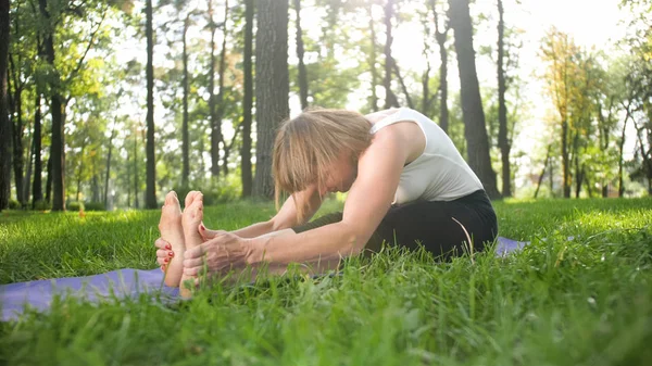 Foto de una mujer sonriente de mediana edad practicando yoga y meditando en el parque. Mujer estirando y haciendo ejercicio en la estera en el bosque — Foto de Stock