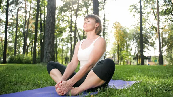 Foto de una mujer sonriente haciendo ejercicios de yoga y fitness. Personas de mediana edad que cuidan de su salud. Armonía del cuerpo y la mente en la naturaleza — Foto de Stock